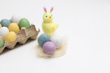 Cute little easter chicken with colorful eggs and yellow flowers on white table