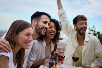 A group of happy humans sitting at a table, with smiles and wine glasses, enjoying leisure time together. The sky above them as they gesture and have fun in a community setting