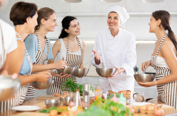 Young female cook holding bowl and whisk in her hands teaching members of cooking course
