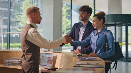 Hotel guests paying contactless with smartphone. Friendly receptionist check in