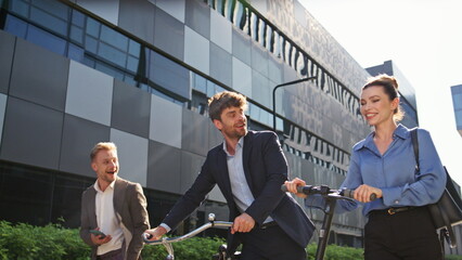 Joyful coworkers going street with eco scooter bicycle. Happy business people