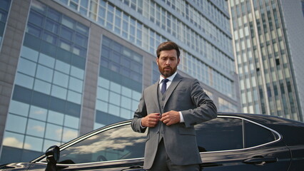 Rich businessman posing car buttoning jacket. Elegant man standing urban street