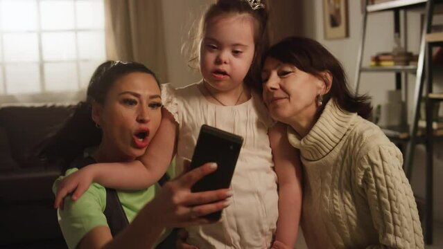 Medium footage of three-generation family of females making selfie with down syndrome child and posing for mobile camera at homeMedium footage of three-generation family of females making selfie with 