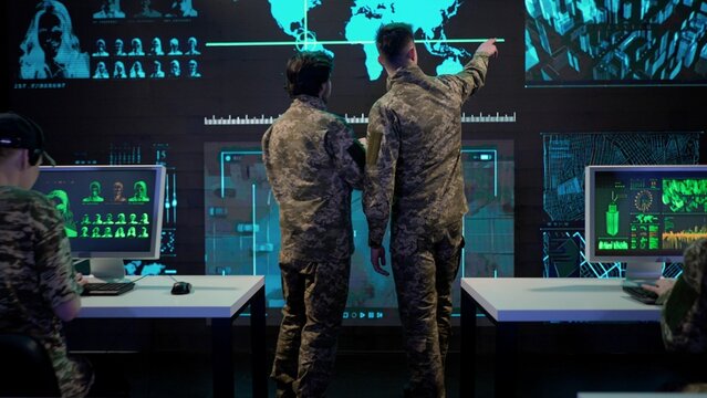 Group of security squad in control center. Military headquarters surveillance officers cyber police working in office, discussing information on a large digital screen. Rear view.