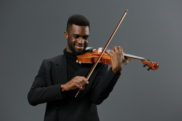 African American musician in black suit playing violin in elegant performance on gray background