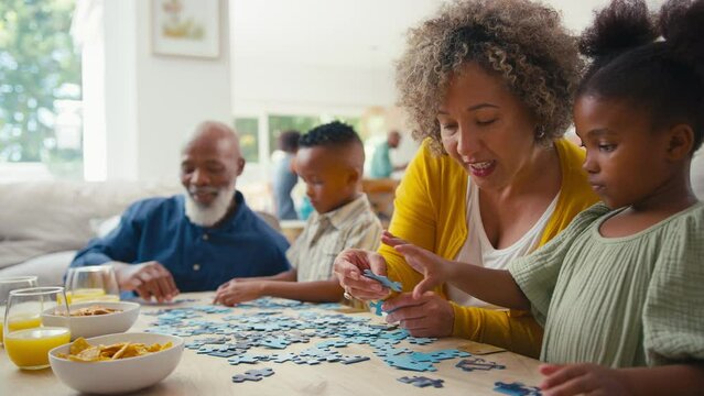 Grandparents with grandchildren indoors at home doing jigsaw puzzle together with parents in background - shot in slow motion