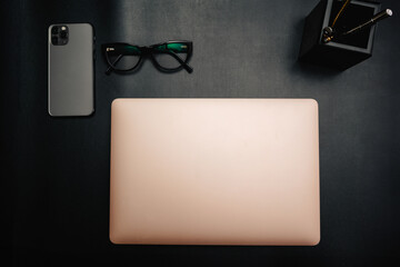 Business layout with items for design. Phone, glasses, pen, laptop on the table. In a dark style, there are object layouts on the table. Top view of items
