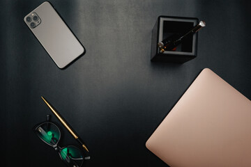 Business layout with items for design. Phone, glasses, pen, laptop on the table. In a dark style, there are object layouts on the table. Top view of items

