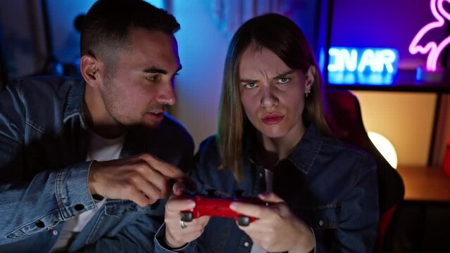 A focused man and woman play video games together in a neon-lit gaming room at night.