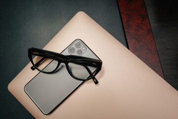 Business layout with items for design. Phone, glasses, pen, laptop on the table. In a dark style, there are object layouts on the table. Top view of items
