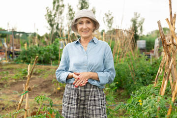 Happy elderly woman posing in her garden, in the backyard of a village house - 769228432