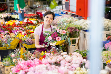 Positive cheerful asian young female florist checking and preparing fresh bouquet with roses and gerberas in flower shop.. - 769229449