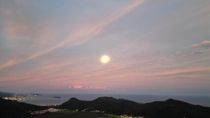 playa con océano iluminada por la Luna, se ve la ciudad a lo lejos, anochecer, Brasil Florianópolis Solidao. (toma aérea).