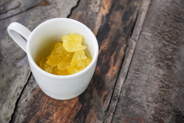 Yellow colored rock sugar in white porcelain cup on wooden table. Coffee or tea drinks sweetener usually used by Javanese people. Empty blank copy text space