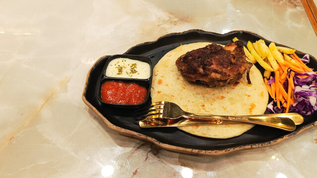 45 degrees of dajaj mashwi, oven roasted chicken (ayam panggang oven) served with 2 khubus (pita bread), french fries, salata, chili sauce and thum with empty space on the side taken closeup