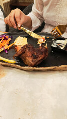 portrait of woman's hands arranging oven-roasted chicken and khubus (pita bread), a typical Arabic food, with a fork and knife on a plate