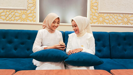 two beautiful Asian women sitting on the sofa smiling cheerfully discussing something on their...