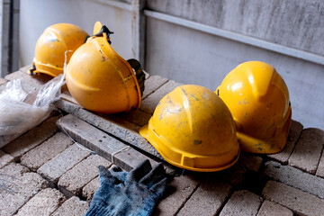 Yellow safety hard hats laying on a pile of bricks in a building construction site.