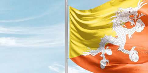 Bhutan national flag with mast at light blue sky.