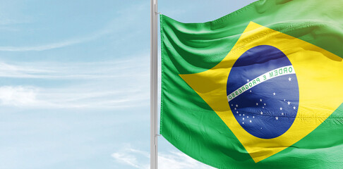 Brazil national flag with mast at light blue sky.