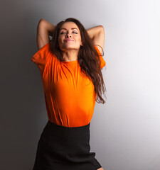 Beautiful young relaxing dreaming smiling woman in casual clothing with closed eyes with arms behind head in orange casual shirt on grey studio background on empty copy space. Closeup - 769242003