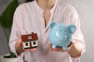 Woman with house model and piggy bank indoors, selective focus