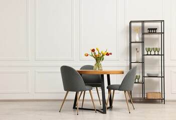 Stylish dining room interior with comfortable furniture and beautiful tulips. Space for text