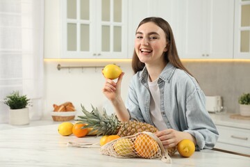 Obraz premium Woman with lemon and string bag of fresh fruits at light marble table in kitchen