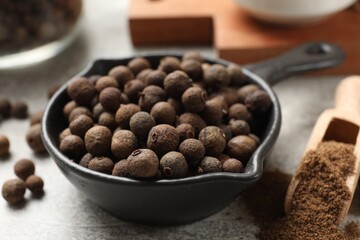 Aromatic allspice pepper grains, powder and scoop on grey table, closeup