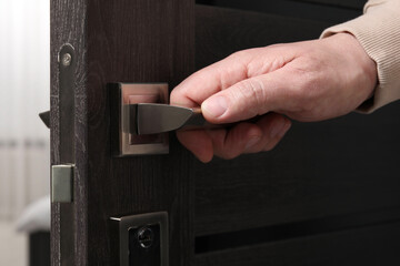 Man opening wooden door indoors, closeup of hand on handle