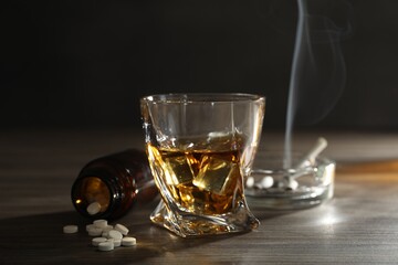 Alcohol addiction. Whiskey in glass, pills and cigarettes on wooden table
