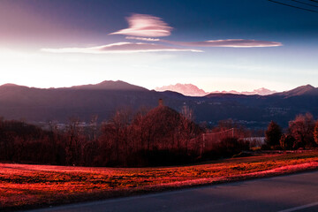 The old tower in the dreamy light of sunset. Country landscape at sunset with Monte Rosa massif and lenticular clouds. (Buccione tower, Piedmont - Italy).