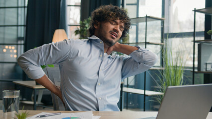 Sick exhausted Arabian Indian latino man feel pain in lower back backache after laptop work unwell ill male guy office manager massaging painful neck relieve ache health problem office syndrome injury