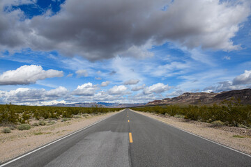 Deserted desert highway stretching to the horizon at midday with distant mountains under a blue sky with cottonball clouds