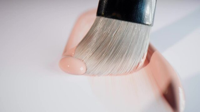 Natural brush spreading base make-up on a white surface, cosmetic product filmed in a packshot studio with a dolly forward movement