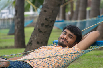 Picture of an Indian person smiling and resting on a hammock at a beach resort. Mahindra resorts, sterling resorts, TAJ hotels, lemon tree, ITC, vacation, garden, trees, knot, family, solo trip, youth