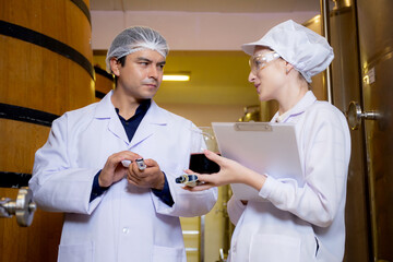 Winemaker team checking and examining producing wine at winery in factory, inspector checking quality and fermenting wine storage in tank or barrel at room, industrial and manufacture concept.