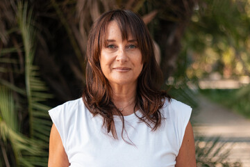 Senior woman about 50 to 60 years old posing and smiling in colorful casual clothes in a park at sunset
