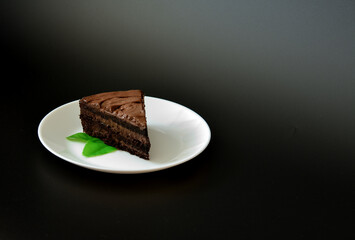 A plate with a piece of chocolate puff cake decorated with mint leaves on a black background.