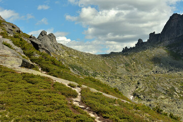 Crossroads of hiking trails on the slope of a high mountain overlooking the pass under a cloudy summer sky.