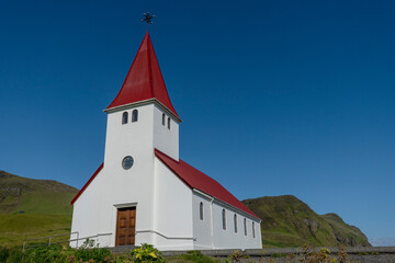 Fototapeta na wymiar Vik i Myrdal Church, little white church with a bright red roof which sits atop a hill above Vík, Iceland. Built in 1929.
