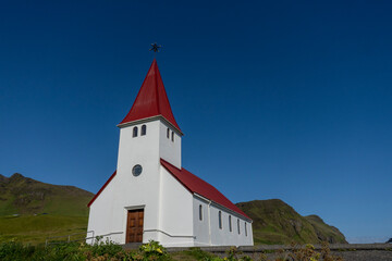 Fototapeta na wymiar Vik i Myrdal Church, little white church with a bright red roof which sits atop a hill above Vík, Iceland. Built in 1929.