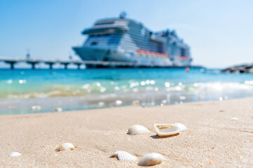 Large blurred cruise liner ship and the seashells in the sand and waves in front. Exotic island...
