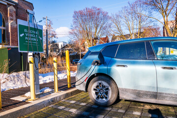 green economy:  electric station wagon / light suv electric vehicle connected  to a charging in a public parking lot shot in toronto beaches in spring - obrazy, fototapety, plakaty