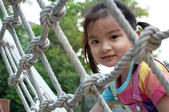 Little girl playing and climb at the playground in the park, nice kid girl on a swing nest, children's learning activities, adventure, looking at camera