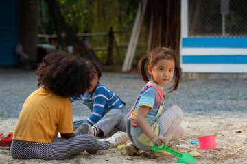 Asian little girl and her African friend play with sand in playground at park, summer outdoor activity for kids