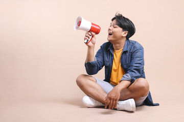 Asian man using megaphones announces good news or discount sale while sitting relax on the floor