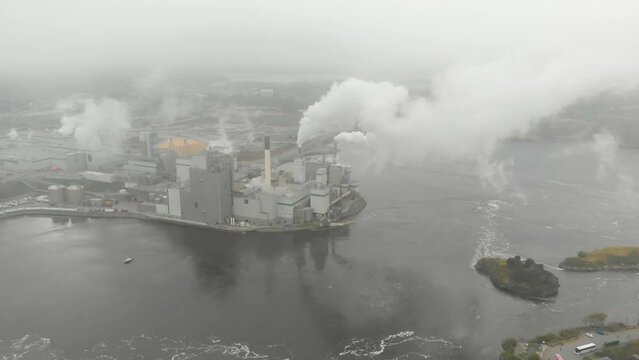 A pull away shot on a cloudy day of the Irving Pulp Factory on the reversing falls as the camera pulls away into the clouds blacking out the screen.