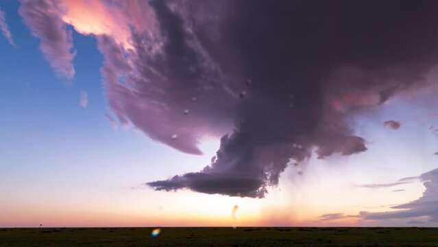A setting sun casts pinks and purples against a decaying supercell thunderstorm.