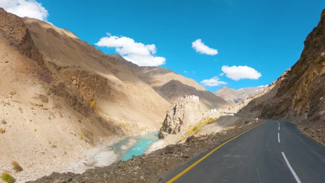 4K shot of Bardan Gompa besides the blue Tsarap river in front of the Himalayan mountains against blue sky with clouds at Zanskar Valley in remote region of Ladakh, India. Monastery besides river.